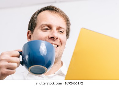 Young man looking at a yellow folder drinking coffee in a blues cup. White background.