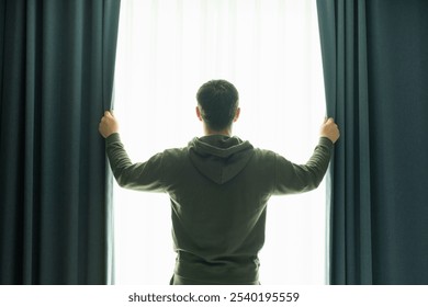 Young man looks out window and opens the curtains, rear view. - Powered by Shutterstock