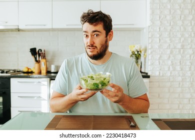 The young man looks with a strange look, as if asking if this should be eaten. How did the guy get tired of fresh juicy greens. Healthy food. Stop diet. Front view.