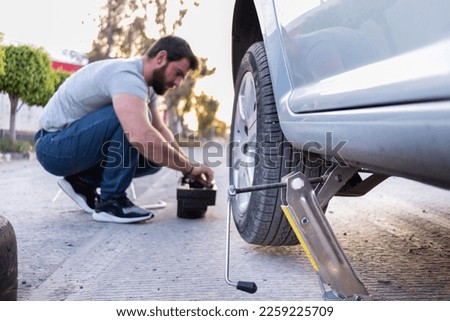 young man loosening a nut of his car tire, changing a flat tire on the road, car jack being used. young man loosening a nut of his car tire, changing a flat tire on the road