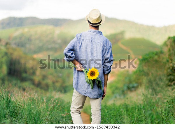 恋人に渡すためにひまわりの花を後ろに隠すのが好きな若い男 の写真素材 今すぐ編集