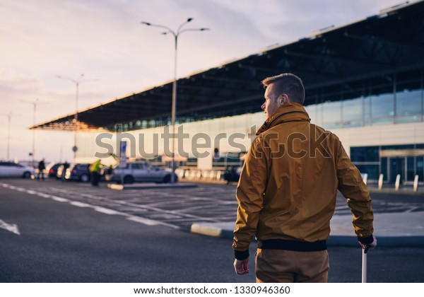 Young man with luggage walking to airport\
terminal at sunrise.