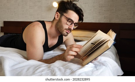 Young Man Lying In Bed And Reading A Book