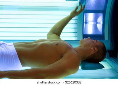 Young Man Lying In Bed  Solarium Adjusts Tanning Booth 