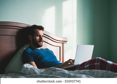 Young man lying in the bed working on a laptop