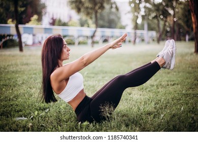 Young Man Lying Down On Green Grass Doing Lower Abs Exercise By Lifting His Legs Up. Sporty Guy Working Out In Park, Side View, Copy Space