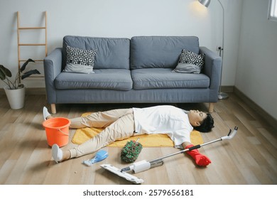Young Man Lying Down On The Floor With Messy Cleaning Tools 