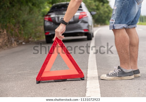 Young man is lying Emergency triangle Put on the\
side of the car parked on the street Travel in the provinces\
Waiting for help From the\
repairs