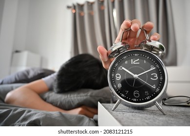 Young man lying on bed and turning off an alarm clock in the morning. - Shutterstock ID 2083121215