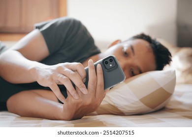 A young man lying on a bed, looking at his smartphone with a thoughtful expression. Relaxed, cozy bedroom setting - Powered by Shutterstock