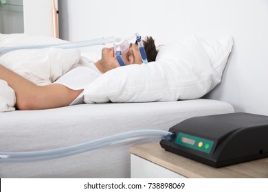 Young Man Lying On Bed With Sleeping Apnea And CPAP