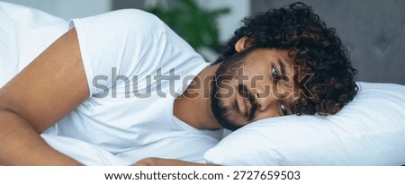 Young Man Lying on Bed Looks Thoughtful While Staring at the Ceiling in a Bedroom Setting