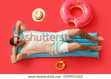 Young man lying on inflatable mattress against color background