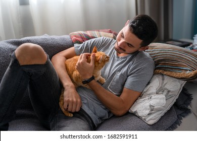 young man lying on a sofa hugs a tabby cat and smiles - Powered by Shutterstock