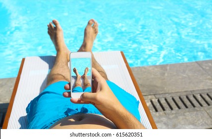 Young Man Lying On Sunbed Near Pool With Phone. Summer Vacation 