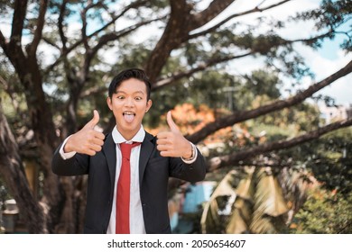 A Young Man Make A Wacky And Crazy Face While Giving Two Thumbs Up Making The Ok Gesture. Posing And Having Fun Outdoors.