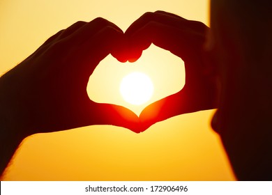 Young man is making heart shape with sun.