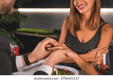 Young man making a proposal while putting on finger an engagement ring to his girlfriend in restaurant. Engagement, new family. She said yes. Present giving sharing