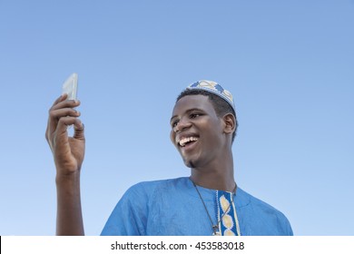 Young man making a self-portrait with his mobile phone under a blue sky   