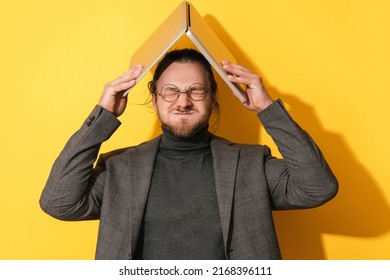 Young man making silly face and holding laptop computer above his head on yellow background