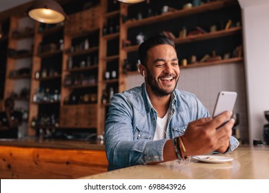 Young Man Making A Video Call From His Mobile Phone. He Is Sitting In Coffee Shop.