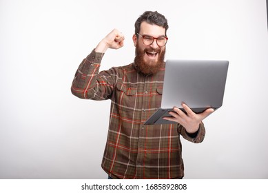 Young Man Is Making Winner Gesture While Looking At His Laptop On White Background