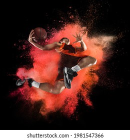 Young Man, Male Basketball Player In Explosion Of Colored Neon Orange Powder Isolated On Dark Black Background. Concept Of Energy, Power, Motion. Copyspace For Ad, Design. Splashing Of Bright Colors.