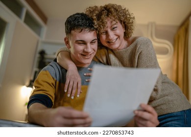 Young man male student teenager and his mother celebrate scholarship read mail letter happy exited smiling reading entry test results success celebrating achievement concept copy space real people