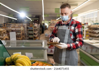 Young Man As A Market Leader With Tablet PC In The Fruit Section In The Supermarket, Employee In Protective Mask Using Digital Tablet In Organic Section Of Supermarket