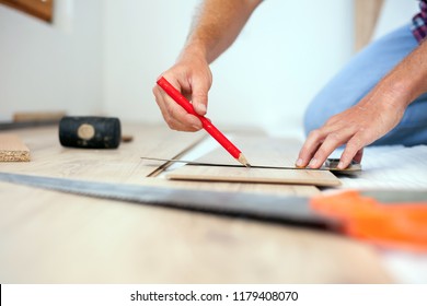 Young Man Measuring And Marking Laminate Floor Tile For Cutting, Installing Laminate Flooring. Close-up Photo With Focus On His Hands. Home Improvement And Renovation Concept