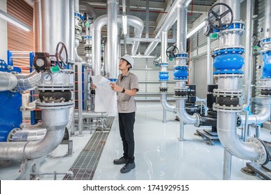 Young Man Mechanical Engineer Holding Drawing To Checking And Inspection Of HVAC Heating Ventilation Air Conditioning System And Pipping Line Of Industrial Construction At Boiler Pump Room System