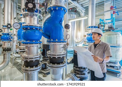 Young Man Mechanical Engineer Holding Drawing To Checking And Inspection Of HVAC Heating Ventilation Air Conditioning System On Pressure Gauge Of Industrial Air Compressor Boiler Pump Room System
