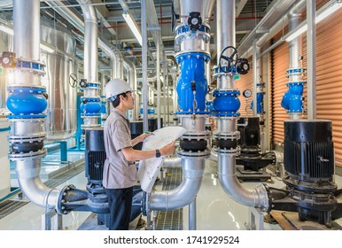 Young man mechanical engineer holding drawing to checking and inspection of HVAC heating ventilation air conditioning system on pressure gauge of industrial air compressor boiler pump room system
