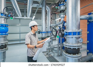 Young Man Mechanical Engineer Holding Drawing To Checking And Inspection Of HVAC Heating Ventilation Air Conditioning System On Pressure Gauge Of Industrial Air Compressor Boiler Pump Room System
