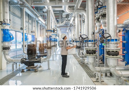 Young man mechanical engineer holding drawing to checking and inspection of HVAC heating ventilation air conditioning system and pipping line of industrial construction at boiler pump room system
