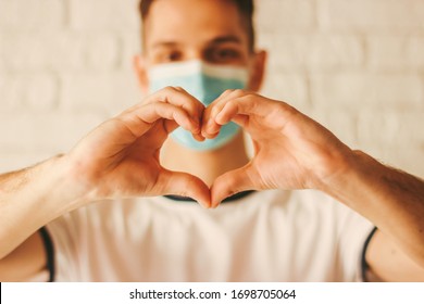 Young Man In Medical Face Mask Gesturing Love Shape Symbol By Hands. Happy Doctor In Protective Mask On Face Holding Fingers In Sign Of Heart. Health Care, Charity, Coronavirus COVID-19, Hands Heart