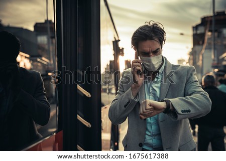 Young man with a medical mask rushing on the bus, looking at his watch, realizing he's late for the curfew - coronavirus protective regulations