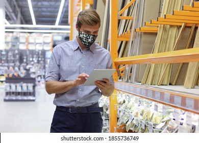 Young Man In Medical Mask Shopping Or Working In A Hardware Warehouse Standing Checking Supplies On His Tablet.