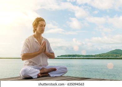 A young man meditates on a rocky beach with a beautiful view of the mountains - Powered by Shutterstock