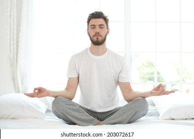Young man meditating in bedroom