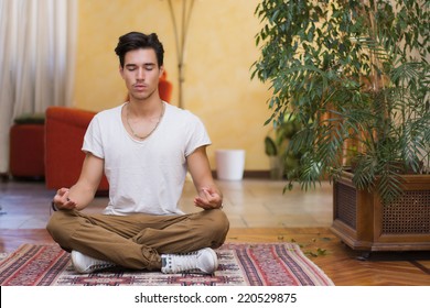 Young man meditating on his living room floor sitting in the lotus position with his eyes closed and an expression of tranquility in a health and fitness concept