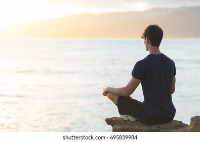 Young man meditating on top ocean cliff during sunset.  - Powered by Shutterstock