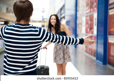 Young Man Meeting His Girlfriend With Opened Arms At Airport Arrival Hall