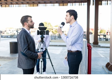 Young man with a microphone interviews a well-dressed celebrity outdoors