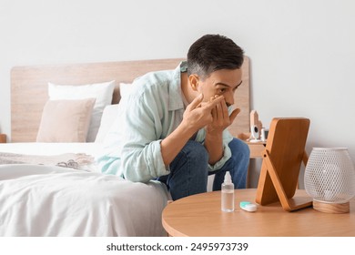 Young man with mirror putting in contact lenses at home - Powered by Shutterstock