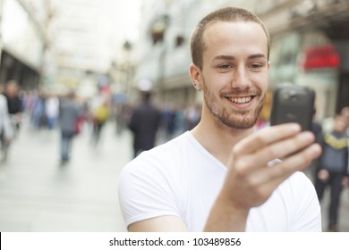 Young Man With Mobile Phone Walking, Background Is Blured City