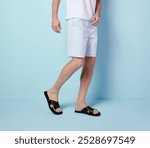 Young man modeling casual summer beachwear, light blue shorts and a white t-shirt with black leather sandals. Navy-inspired casual style, highlighting tanned legs and a relaxed, fashionable beach vibe