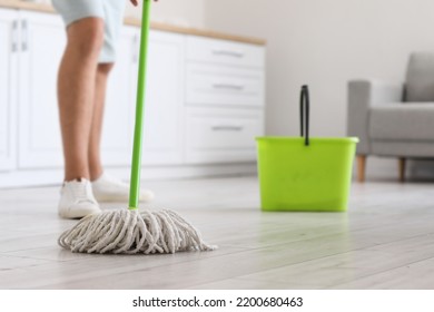 Young man mopping floor in modern kitchen, closeup