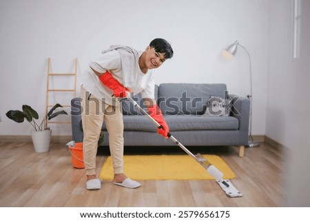 Young Man Mopping The Floor While Smiling At Camera Enjoying House Chores