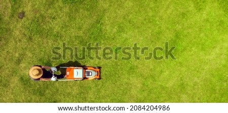 A young man is mowing a lawn with a lawn mower in his beautiful green floral summer garden. A professional gardener with a lawnmower cares for the grass, view from above